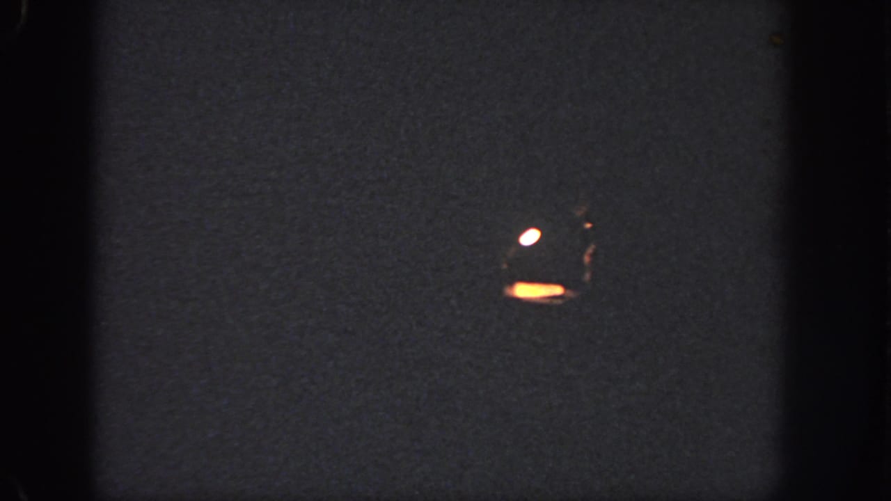 Low-light Georgia 8mm frame showing a small bright shape near dark water or ground, with surrounding grain and heavy shadow.