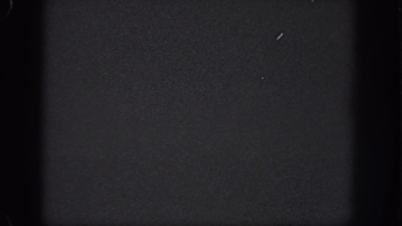 Near-black 1951 Georgia-sourced 8mm frame with dense grain, dark gate edges, and small surface specks.