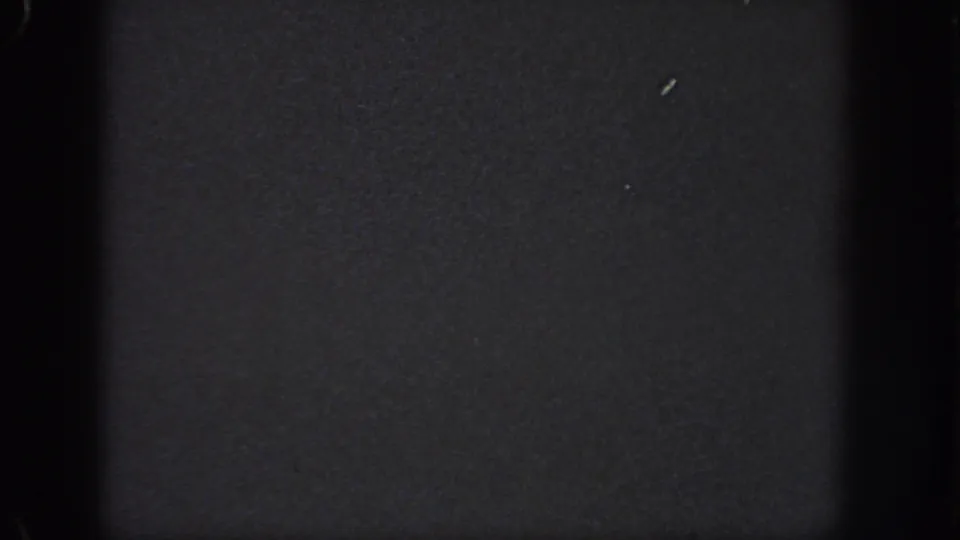 Near-black 1951 Georgia-sourced 8mm frame with dense grain, dark gate edges, and small surface specks.
