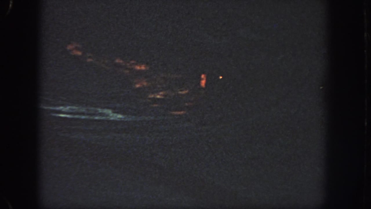 Dark 1951 Georgia-sourced 8mm frame with faint orange light leakage, a bluish streak, grain, and gate-edge shadows.
