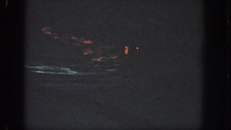 Dark 1951 Georgia-sourced 8mm frame with faint orange light leakage, a bluish streak, grain, and gate-edge shadows.