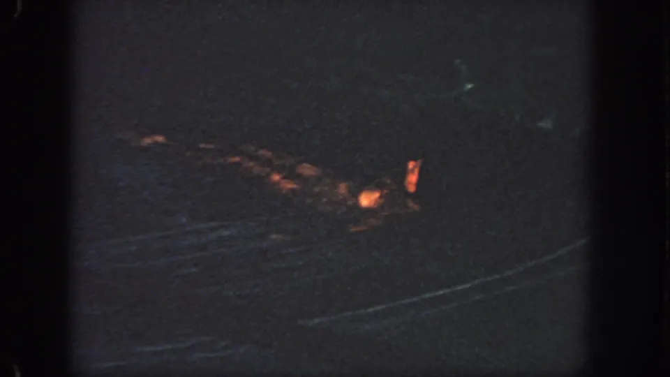Distant night view of dark water with an orange life jacket or flotation shape visible near the surface.
