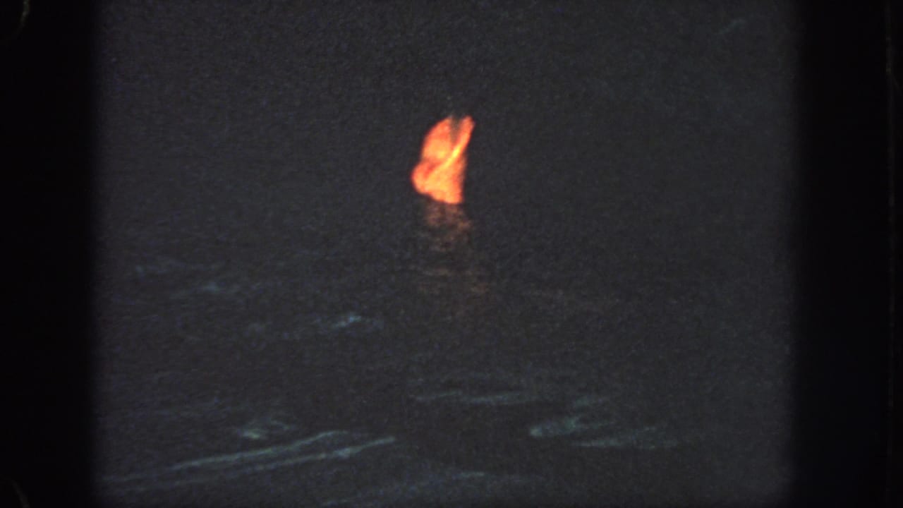 A distant person appears partly visible in dark offshore water, marked by a bright orange life jacket or flotation device.