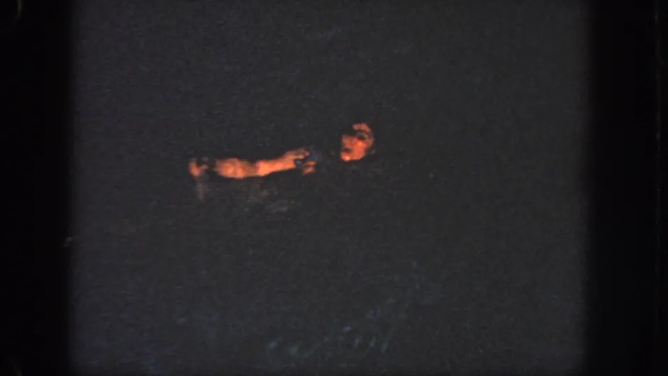 1951 Georgia 8mm frame showing the swimmer lower in the dark pool, with her face and arm softly lit against the water.