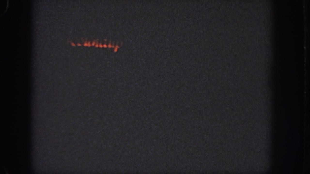 Dark 8mm frame with faint orange lights near the upper left and heavy black borders.