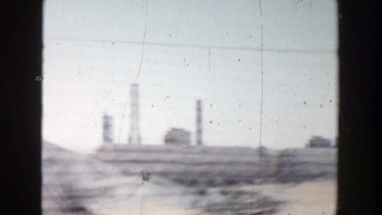 Vehicle-pass-by view in Grand Rapids, Michigan, with hazy smokestacks, low structures, stacked material, and visible 8mm dust and scratches.