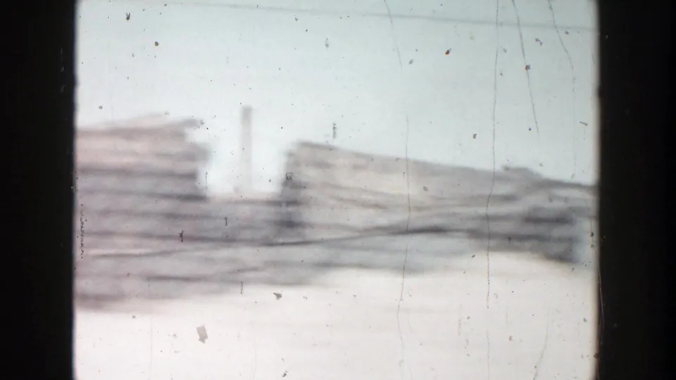 Final 8mm frame from the moving vehicle, showing hazy stacked materials, low industrial forms, and vertical pipes or smokestacks in Grand Rapids.