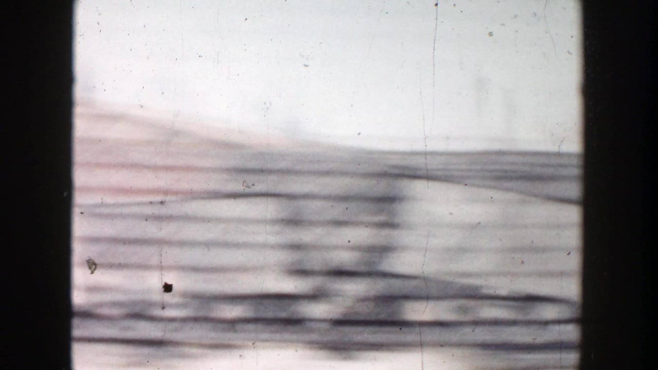 1956 Grand Rapids home-movie frame showing a fast, blurred vehicle-window view of wires and industrial roadside forms.