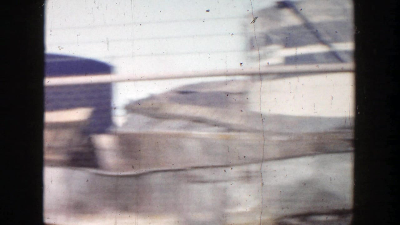 A blurry 1956 Grand Rapids street view with a rounded industrial tank-like form passing behind dark window bars.