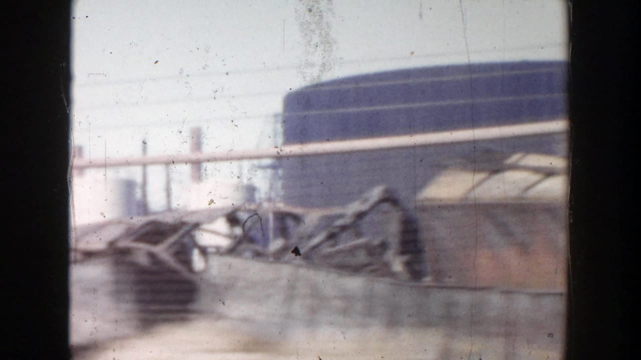 A 1956 Grand Rapids vehicle-window frame showing blurred industrial buildings and low roadside barriers.