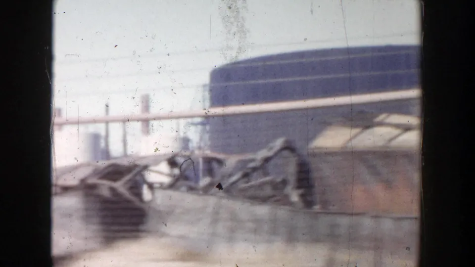 A 1956 Grand Rapids vehicle-window frame showing blurred industrial buildings and low roadside barriers.