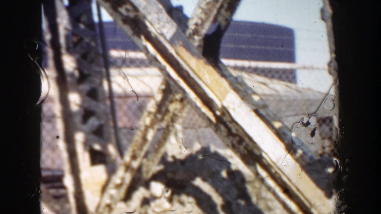 1956 Grand Rapids home-movie frame showing an obstructed roadside construction view with steel members, pale material, and film dust.