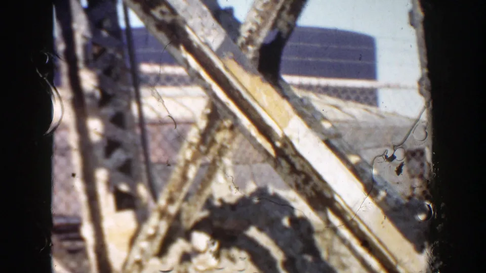 1956 Grand Rapids home-movie frame showing an obstructed roadside construction view with steel members, pale material, and film dust.