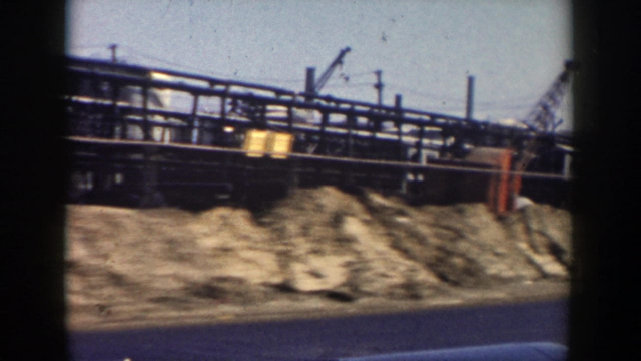 Grand Rapids roadside construction area with dirt piles, elevated industrial piping, utility poles, and the lower edge of a vehicle window.
