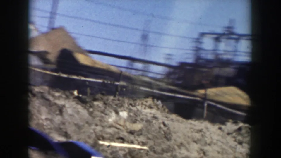 Passing 1956 Grand Rapids view with dirt piles, power lines, railings, and industrial framework under a bright sky.