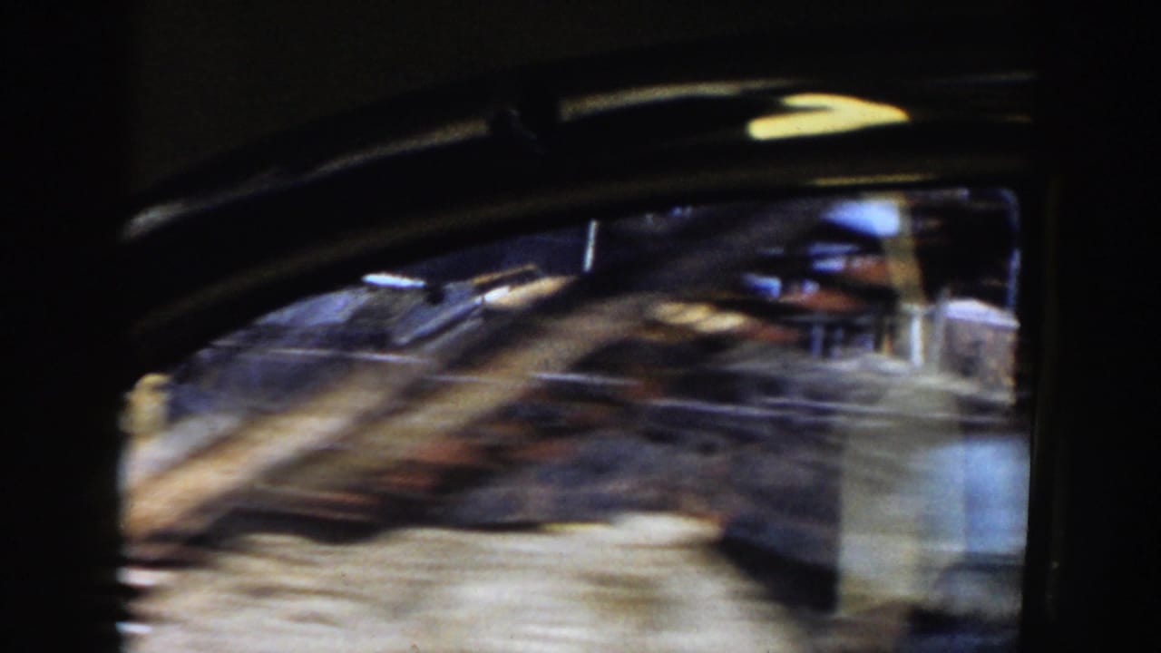 Blurred view through a vehicle window passing a house or yard structure.