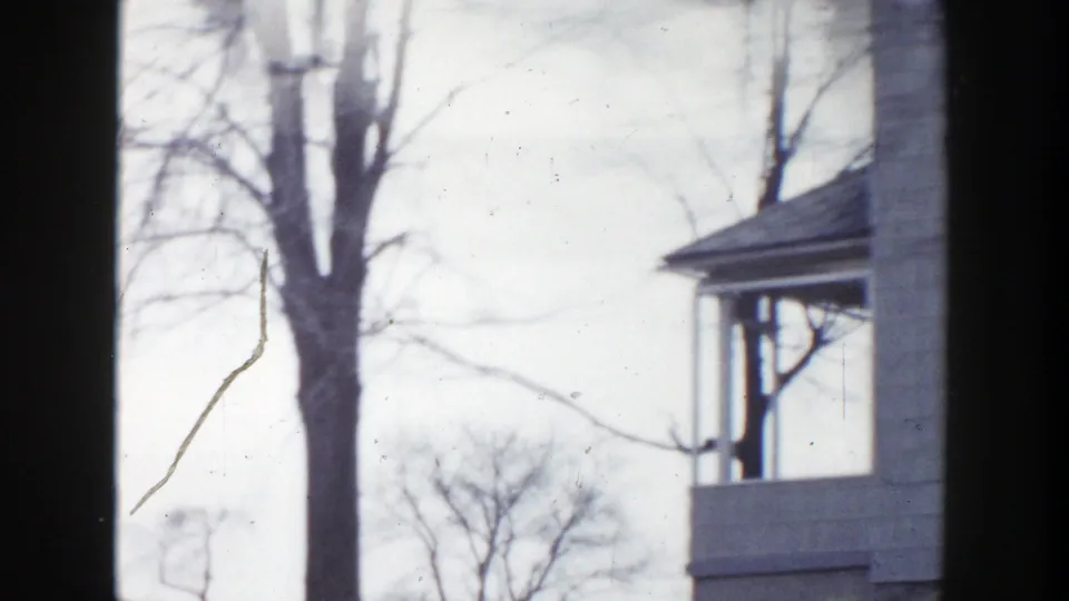 The final 1956 Grand Rapids frame shows a bare tree, pale sky, and the edge of a porch or house as the car continues past.