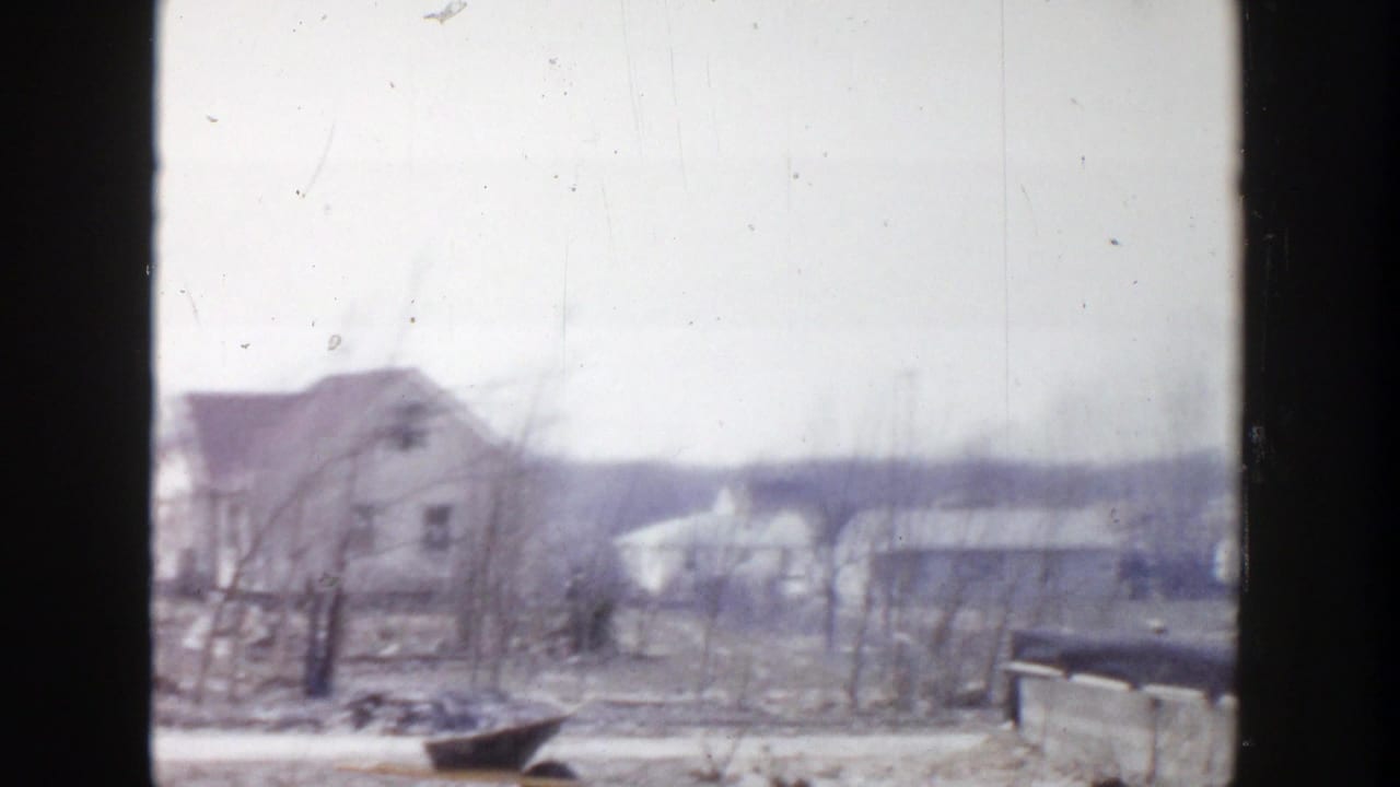 1956 Grand Rapids 8mm frame showing a soft, overcast view of houses, bare trees, low rooftops, and distant ground.