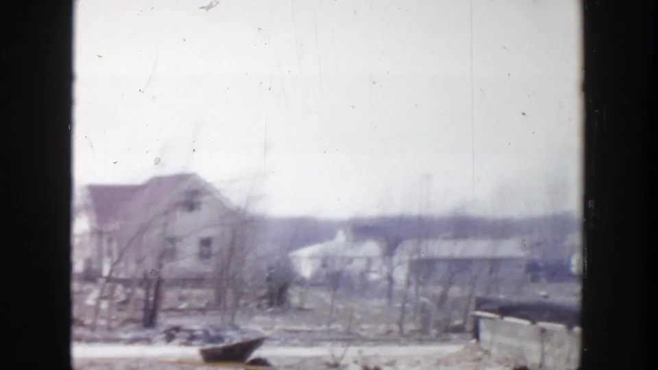 1956 Grand Rapids 8mm frame showing a soft, overcast view of houses, bare trees, low rooftops, and distant ground.