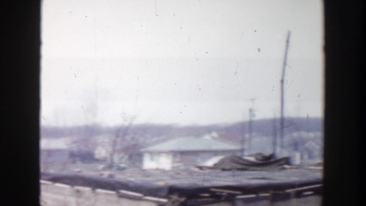 1956 Grand Rapids 8mm frame looking across rooftops, a utility pole, bare trees, and distant low buildings in soft focus.