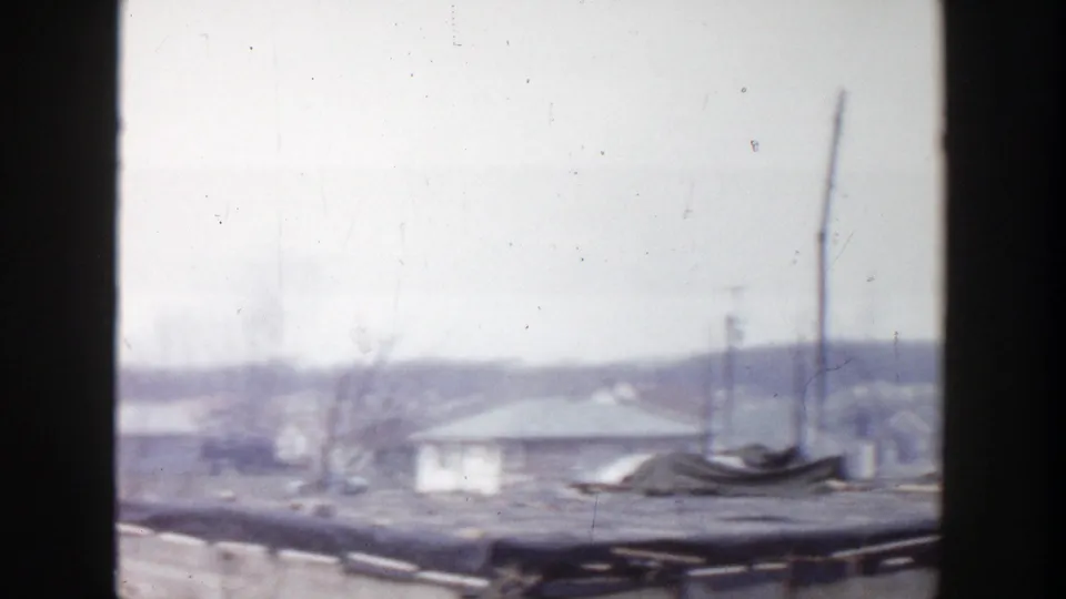 1956 Grand Rapids 8mm frame looking across rooftops, a utility pole, bare trees, and distant low buildings in soft focus.