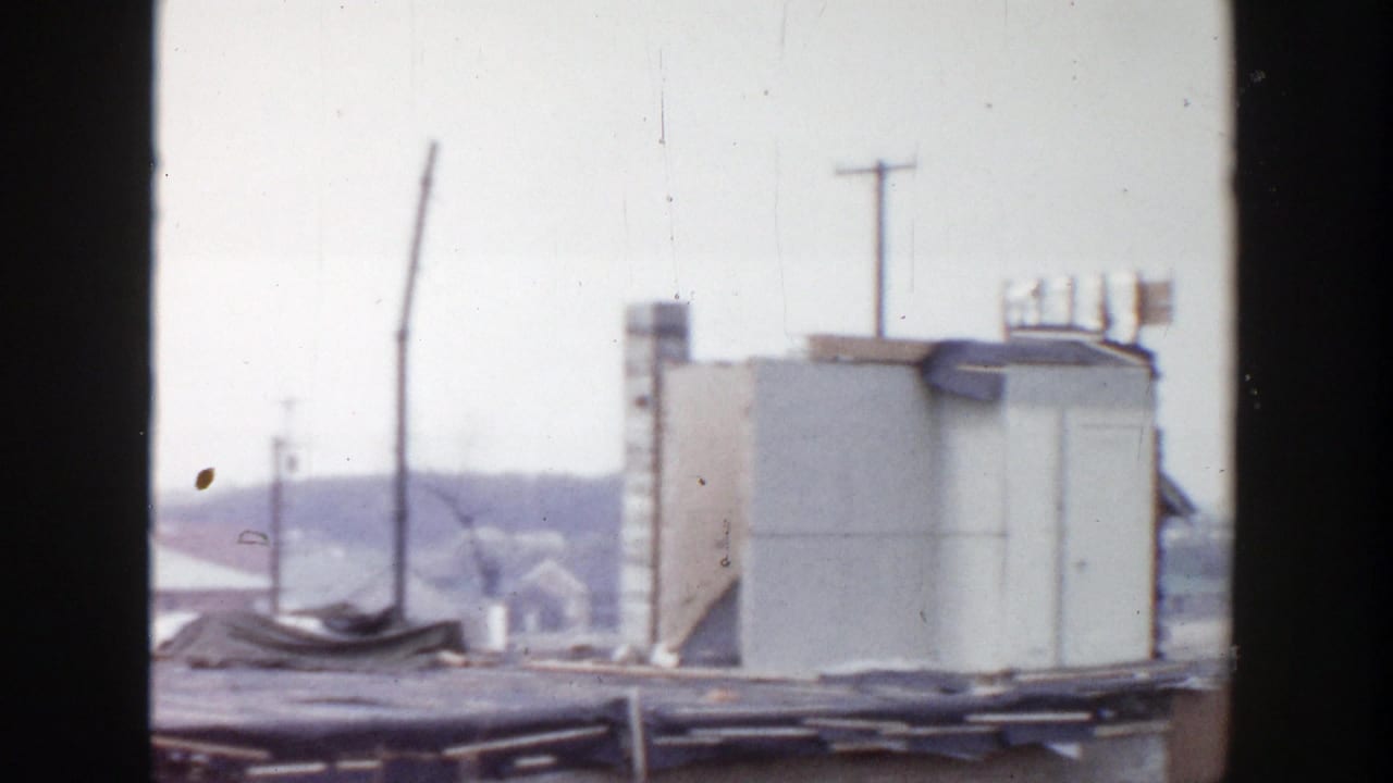 1956 Grand Rapids 8mm frame centered on a pale rooftop structure, utility poles, roof edges, and distant houses.