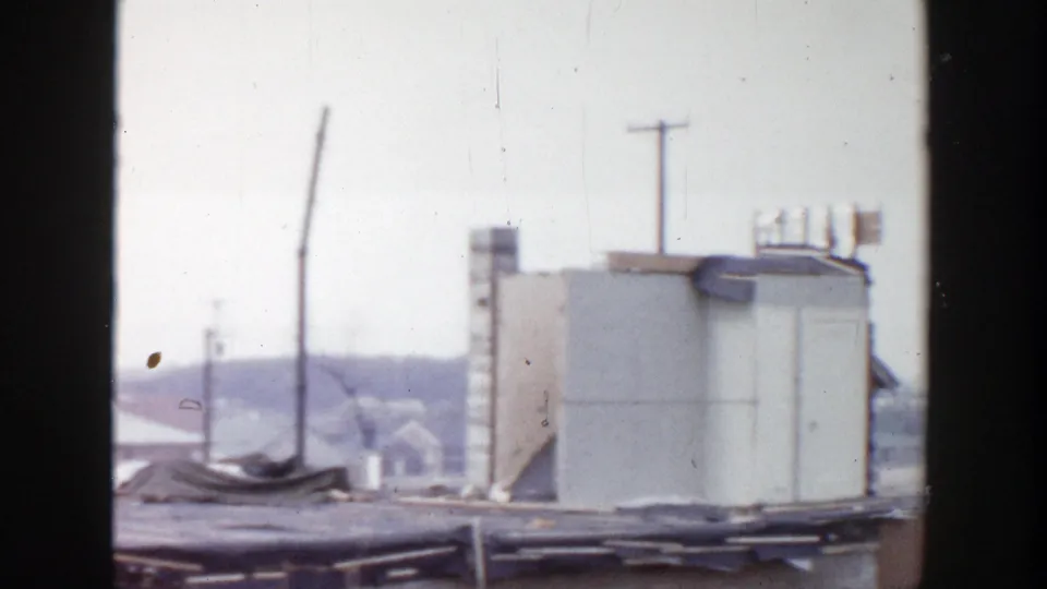 1956 Grand Rapids 8mm frame centered on a pale rooftop structure, utility poles, roof edges, and distant houses.