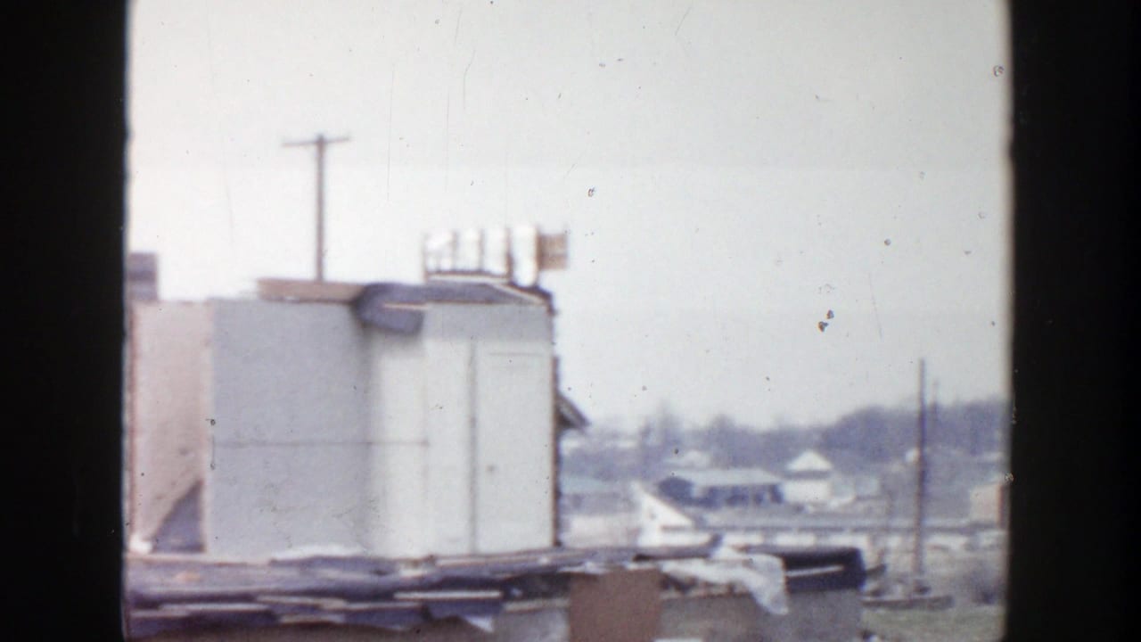 1956 Grand Rapids 8mm frame showing a rooftop structure, surrounding roofline, utility poles, and distant low houses.