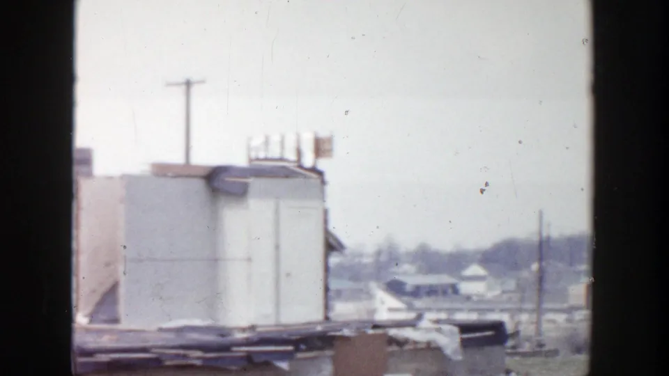 1956 Grand Rapids 8mm frame showing a rooftop structure, surrounding roofline, utility poles, and distant low houses.