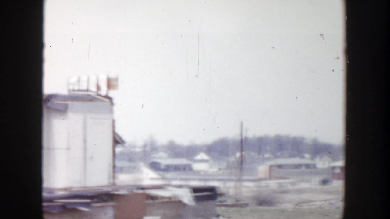 Distant industrial lot with a large tank or trailer structure and low buildings under a pale sky.