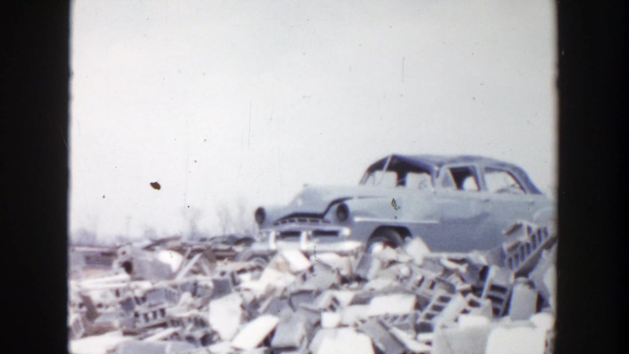 A worn 1950s sedan sits above piles of broken masonry and scattered debris.
