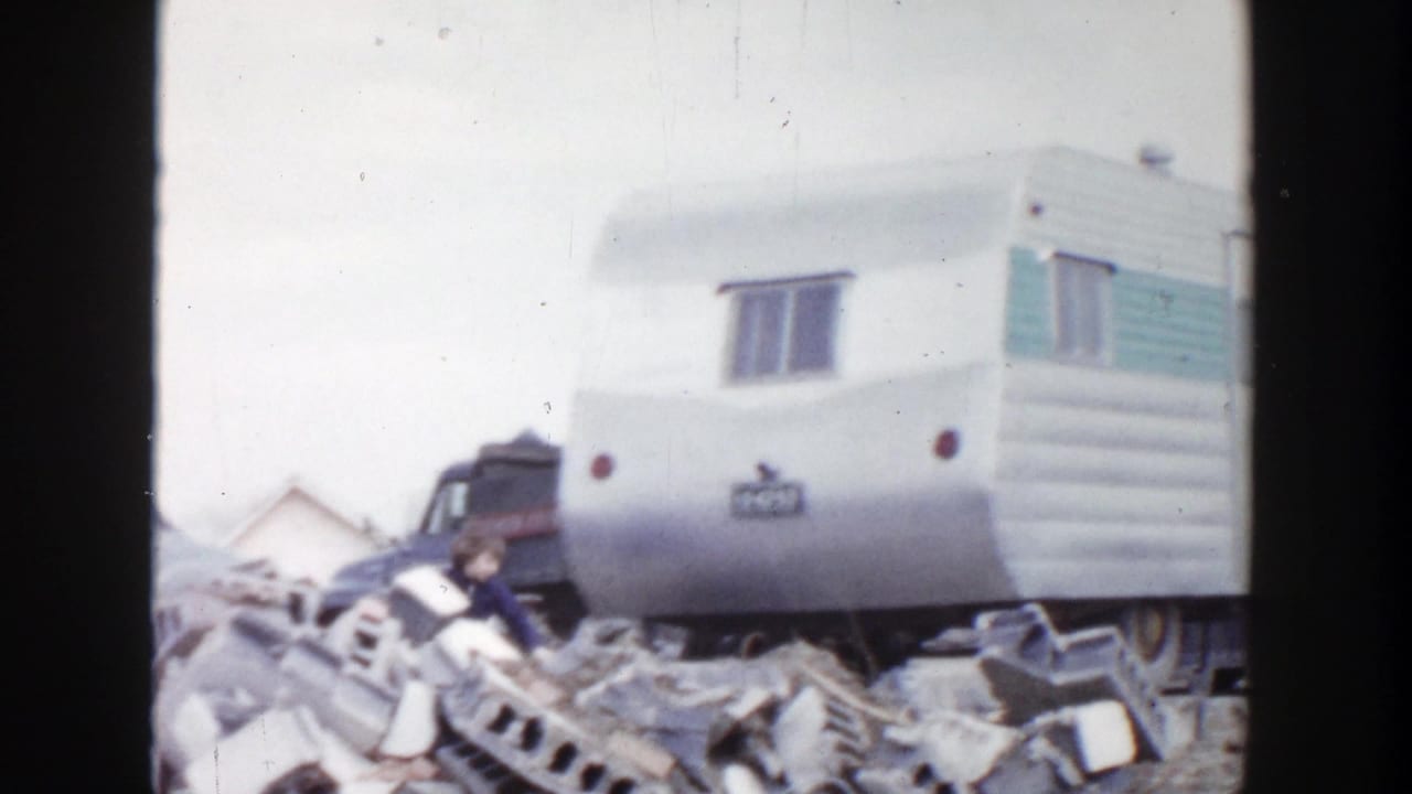 1956 Grand Rapids home-movie frame showing a white camper with teal trim surrounded by broken blocks and debris.
