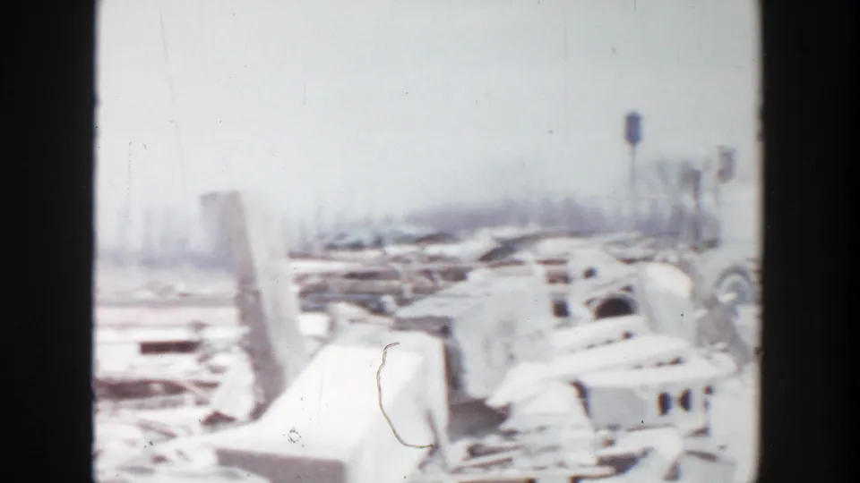 1956 Grand Rapids frame showing a wider debris field with cinder blocks, broken boards, and distant posts or utility structures.