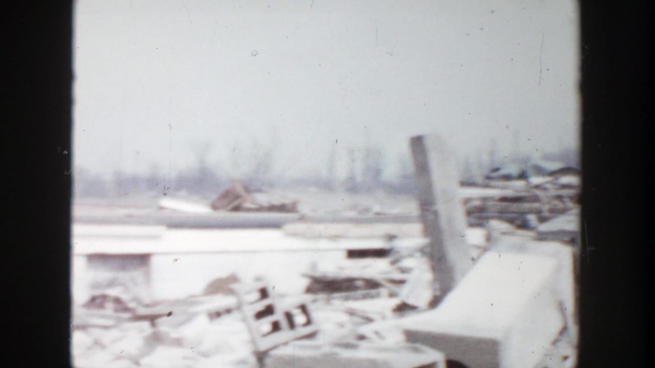 1956 Grand Rapids 8mm frame showing scattered rubble, collapsed material, and part of a damaged low building in an open area.
