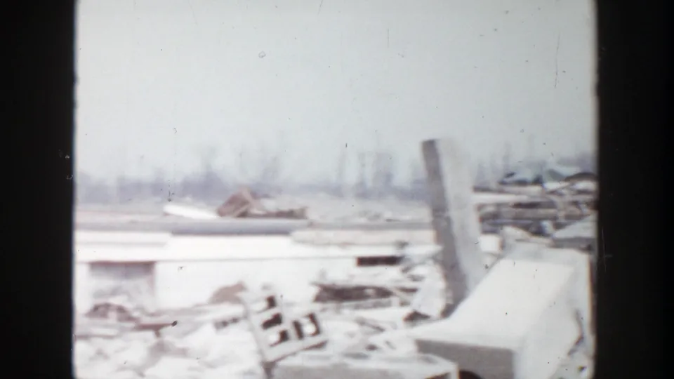1956 Grand Rapids 8mm frame showing scattered rubble, collapsed material, and part of a damaged low building in an open area.