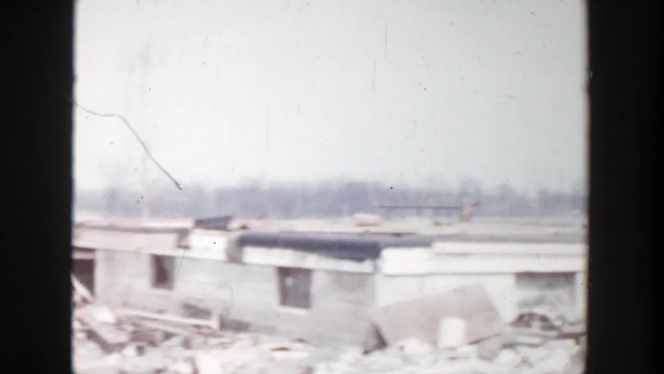 1956 Grand Rapids home-movie frame showing a damaged low structure, broken material, and debris scattered across the site.