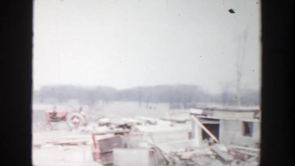 1956 Grand Rapids 8mm frame showing a tractor, rubble, and a low damaged structure across an open rural or suburban site.