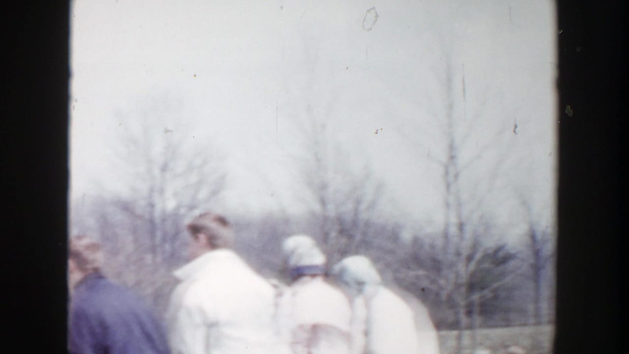 Adults in heavy coats walk through a winter neighborhood setting in Grand Rapids, Michigan, in 1956 home-movie footage.