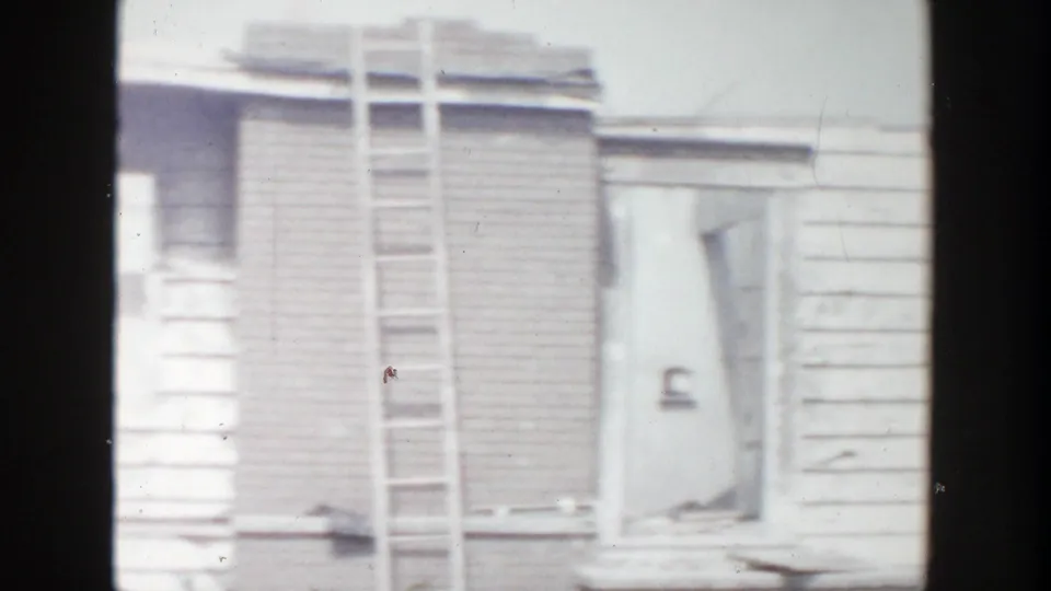 A damaged Grand Rapids house exterior shows broken window areas, missing siding, and a ladder leaning against the structure.