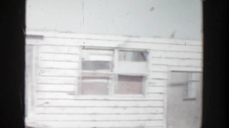 The 8mm frame shows a Grand Rapids residential exterior with damaged siding, broken windows, and pale winter light.