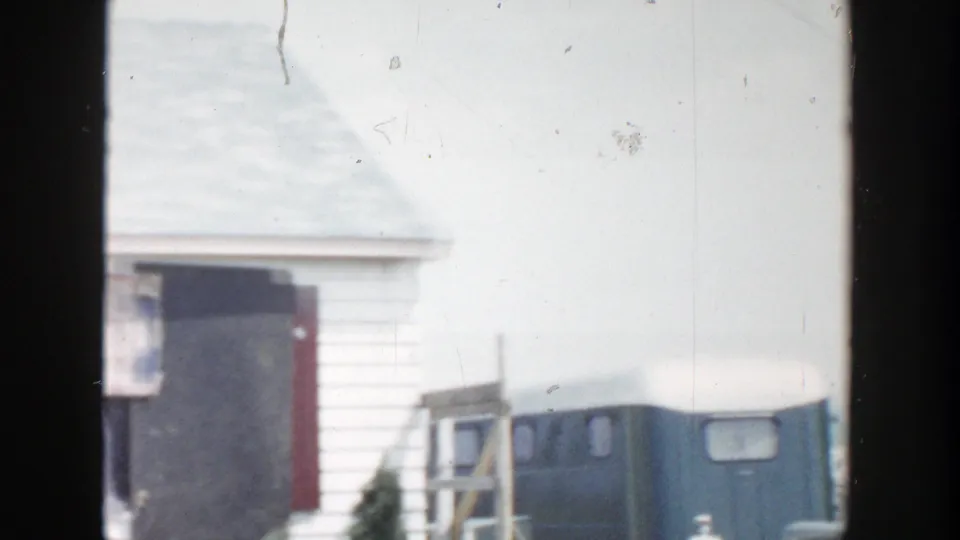 1956 Grand Rapids frame showing a white residential exterior, dark doorway, steps, ladder or railing, and a small blue outbuilding.
