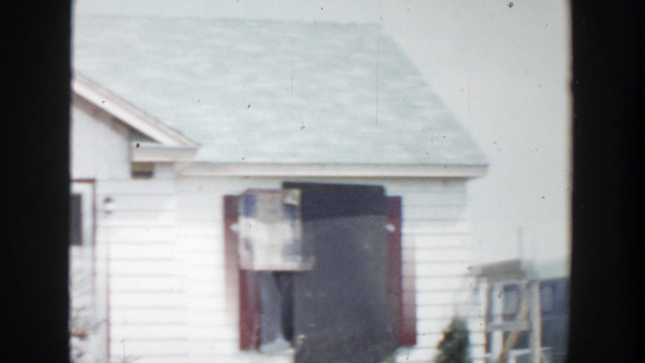 White house exterior with red trim and a dark boarded window opening.
