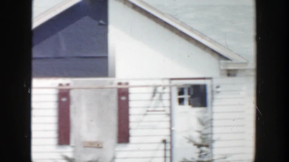 1956 Grand Rapids frame showing a white house facade with red shutters, a pale door, and a dark damaged upper section.