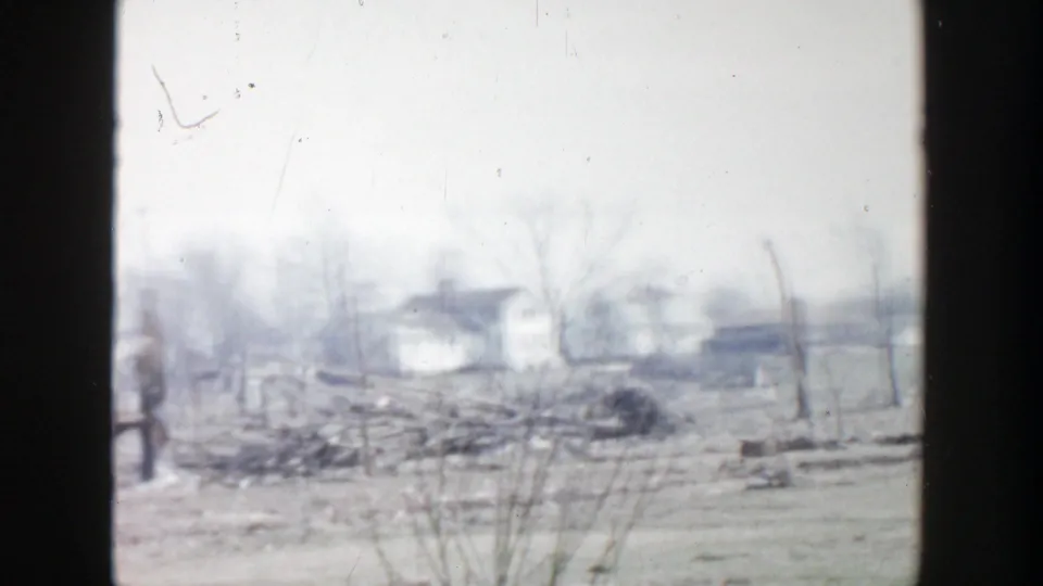 1956 Grand Rapids home-movie view of a bare residential yard with scattered debris, fencing, and distant structures.