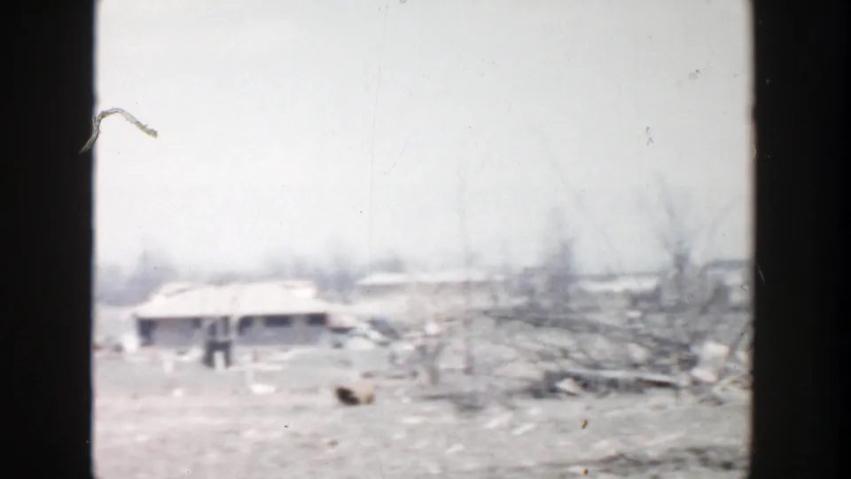1956 Grand Rapids-area frame showing a low farm building, bare earth, scattered debris, and leafless trees in a muted 8mm view.