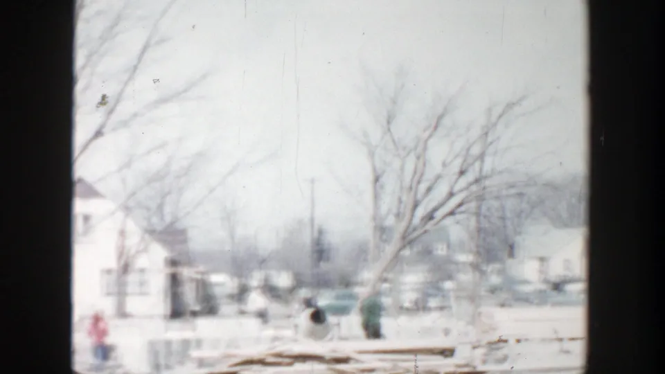 Grand Rapids winter residential scene with a prominent leafless tree, bundled people walking, snow-covered ground, and houses in the background.