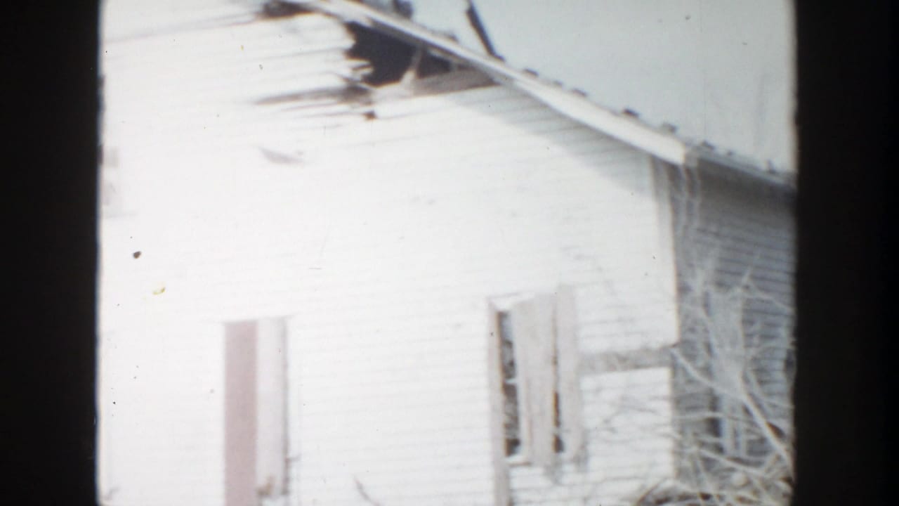 Overexposed white house wall with a broken window, damaged roof area, and film border.