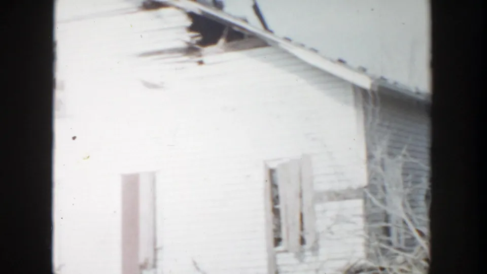 1956 Grand Rapids 8mm frame focused on the upper white house wall, with a broken window and dark roof damage near the eaves.