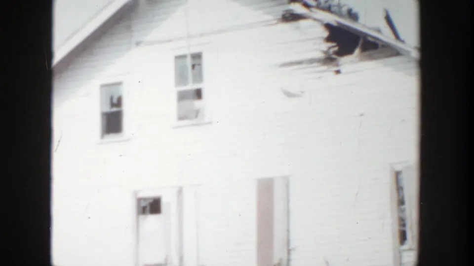 1956 Grand Rapids 8mm frame showing more of the white house facade, including upper windows, a boarded lower opening, and damaged roof material.