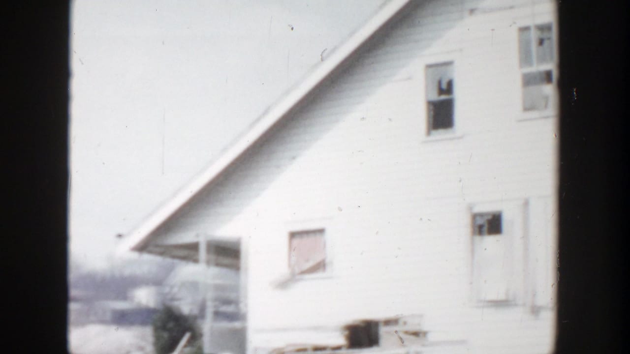 White clapboard house with boarded window and dark film-frame borders.